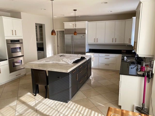 Modern kitchen with white cabinets, dark island, stainless steel appliances, and tiled floor.