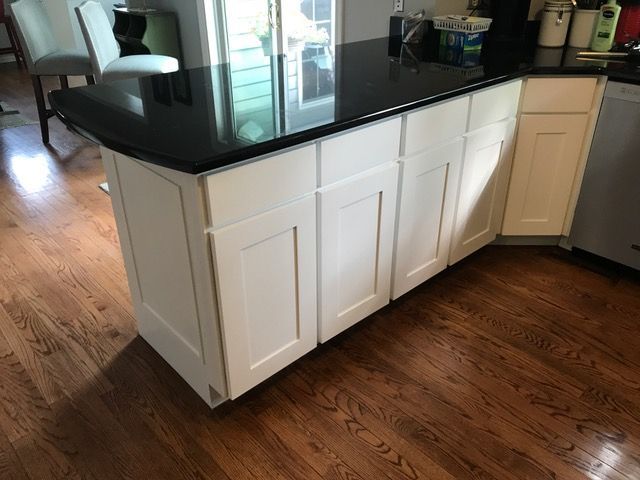 White kitchen island with a black countertop and hardwood floors.