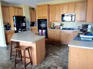 Kitchen with light wood cabinets, dark appliances, tile floor, and an island with stools.