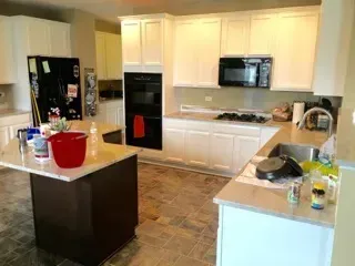 Kitchen with white cabinets, dark island, appliances, and tan countertops.