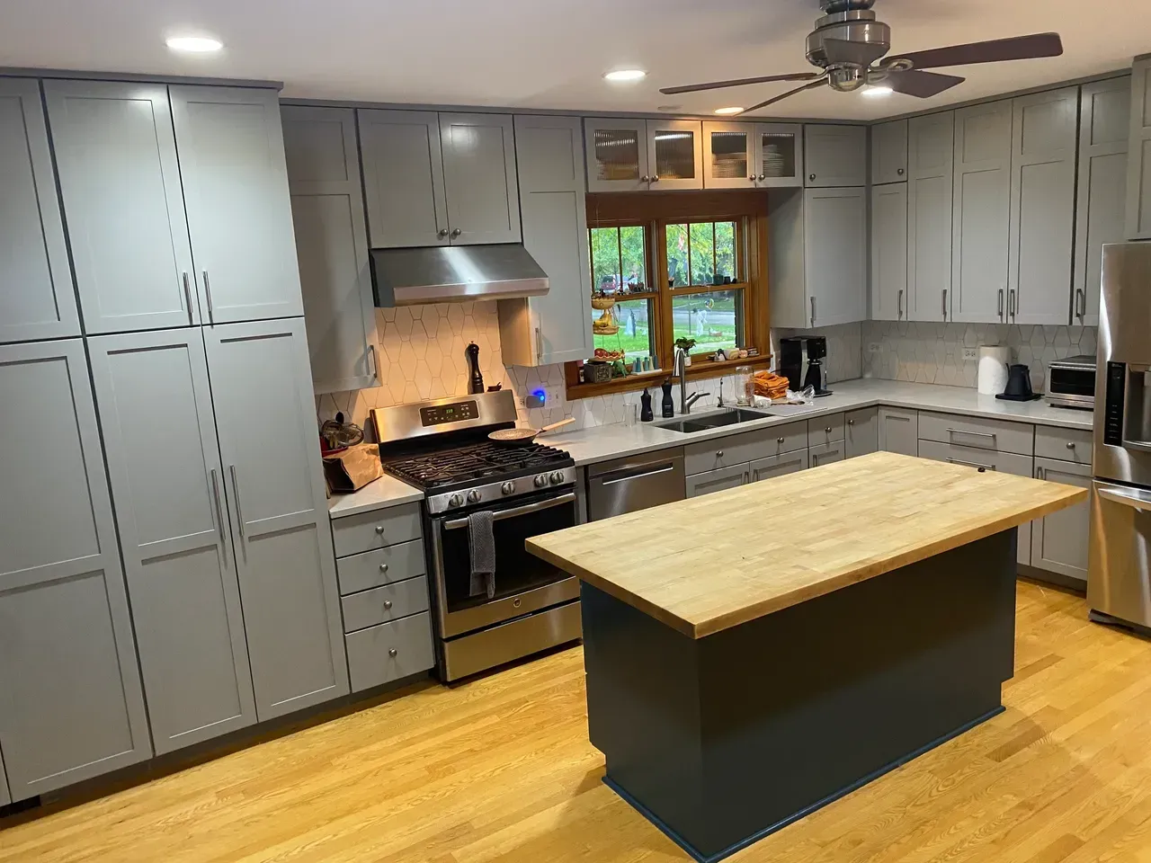 Gray kitchen cabinets with a butcher block island. Stainless steel appliances and light wood floors.