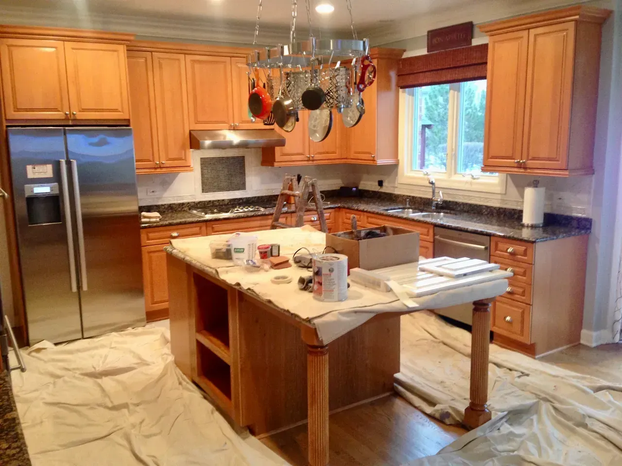 Kitchen with wood cabinets, stainless steel appliances, and an island covered in painting supplies.
