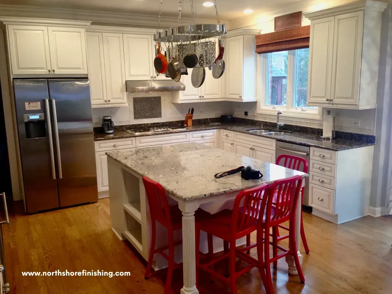 White kitchen with granite countertops, stainless steel appliances, and red bar stools.