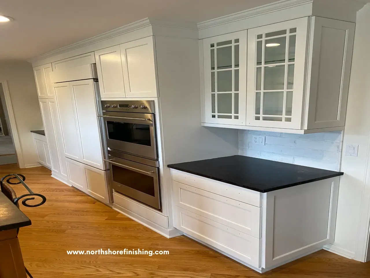White kitchen cabinets with appliances and black countertop on hardwood floor.