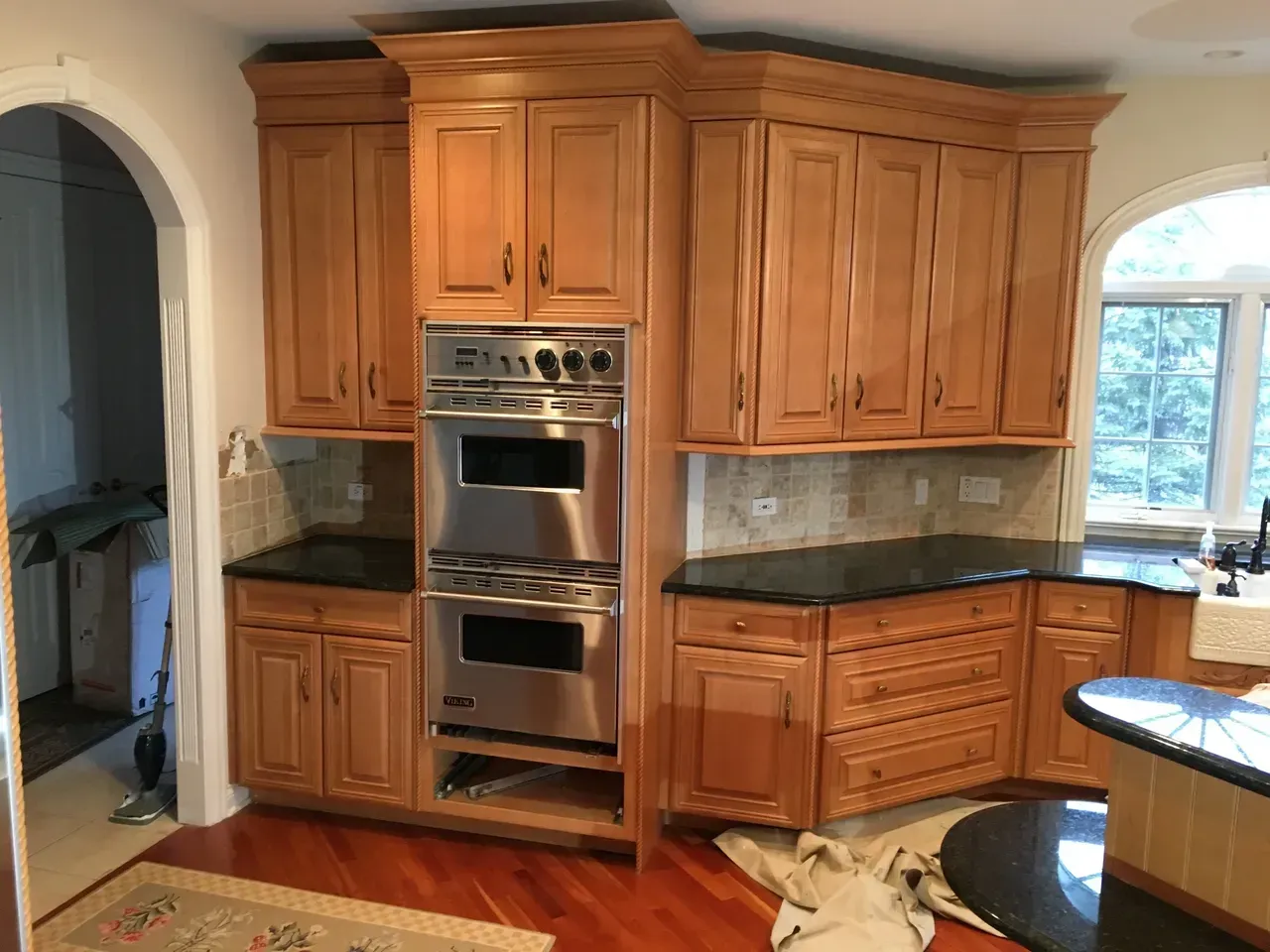 Kitchen cabinets with stainless steel oven, black countertops, and wooden floors.
