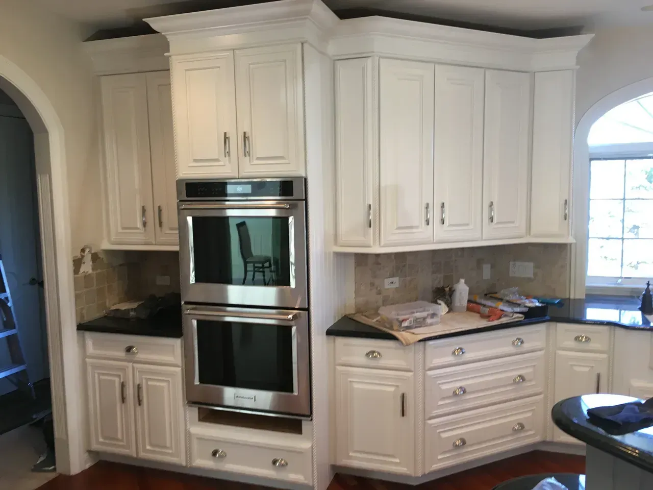 White kitchen cabinets with black countertops and stainless steel oven built-in.