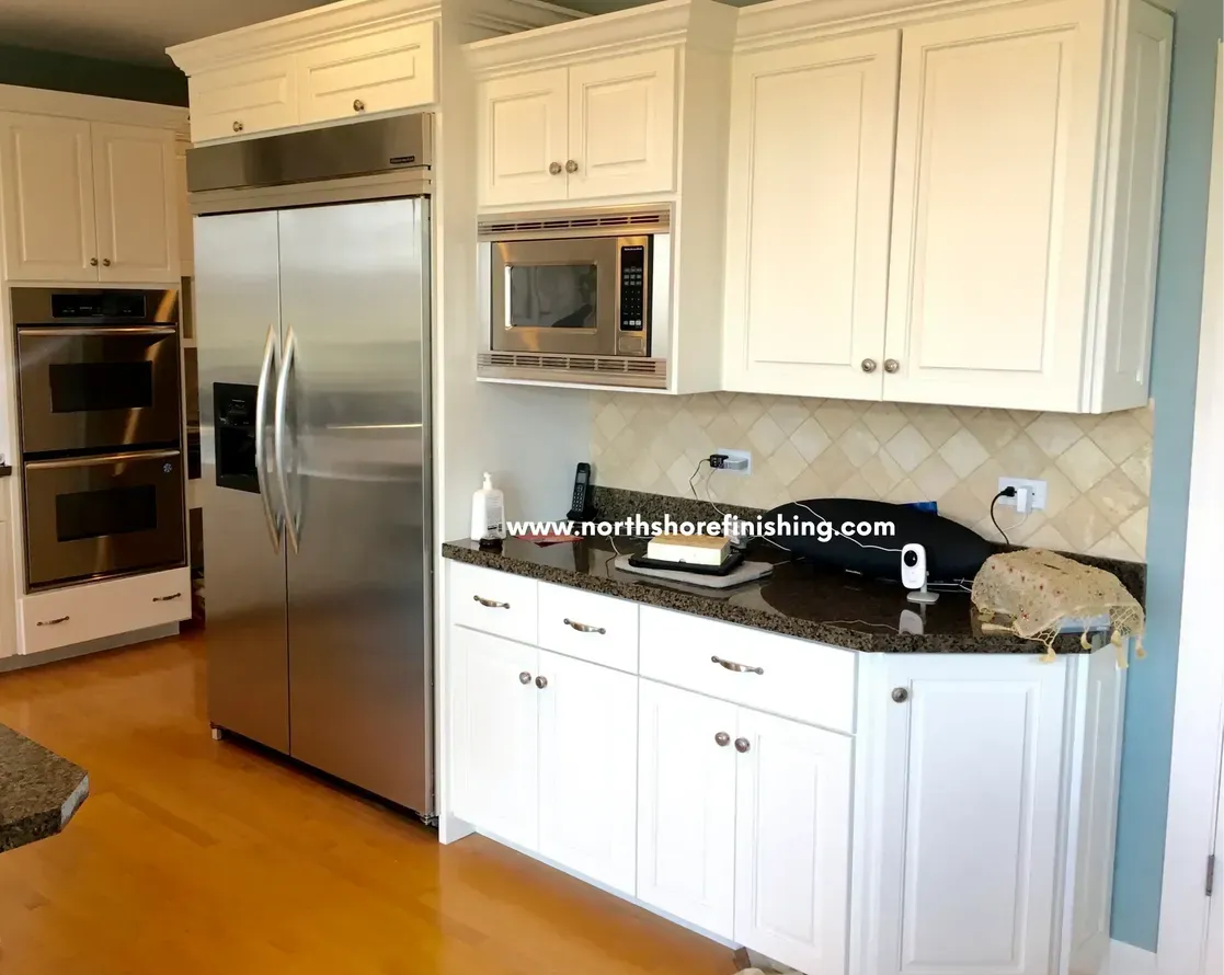 White kitchen with stainless steel appliances, dark countertops, and light wood flooring.