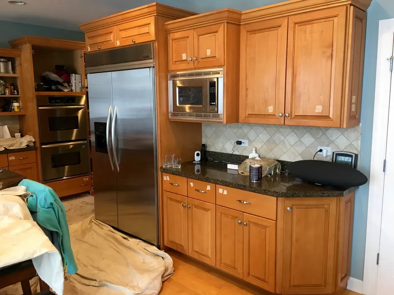 Kitchen with stainless steel refrigerator, wooden cabinets, microwave, and granite countertop.