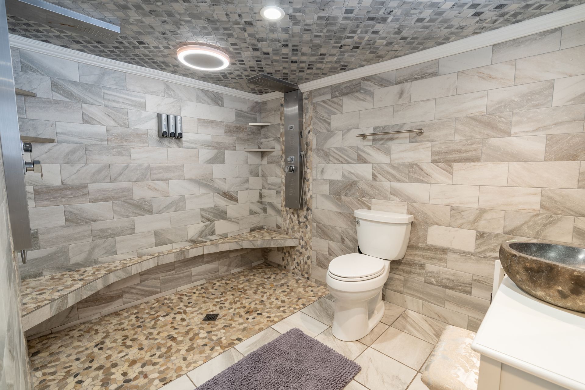Bathroom with tiled walls, pebble floor, built-in bench shower, and a toilet.