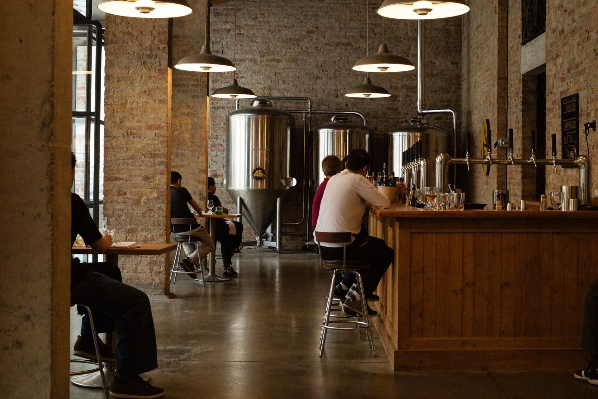 A craft brewery taproom inside a historic brick building with fermentation tanks and a row of tap handles in Gainesville