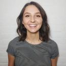 Woman smiling, wearing a striped shirt, standing against a white wall.