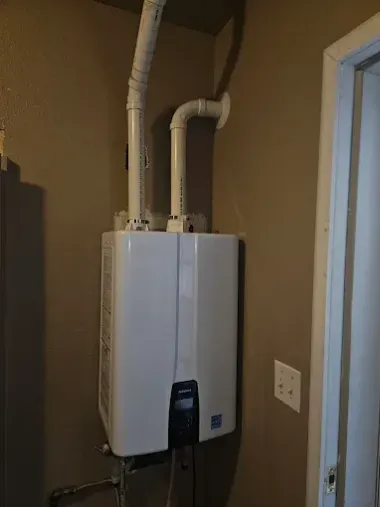 Wall-mounted white boiler with two insulated pipes in a small utility room near a door