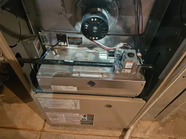 Interior view of a furnace with exposed wiring, blower, and metal panels, showing the HVAC unit inside a closet.