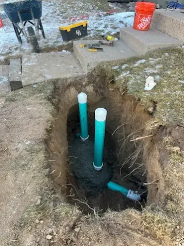 Open trench with three blue PVC pipes and construction tools on dirt ground