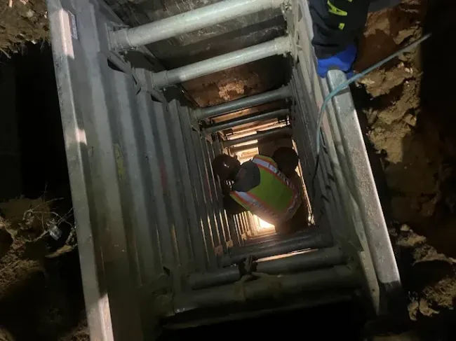 Worker descending a metal ladder inside a narrow vertical shaft during construction work