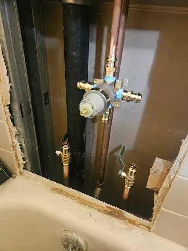 Open wall plumbing with brass pipes and a gray valve assembly on dark insulated pipes