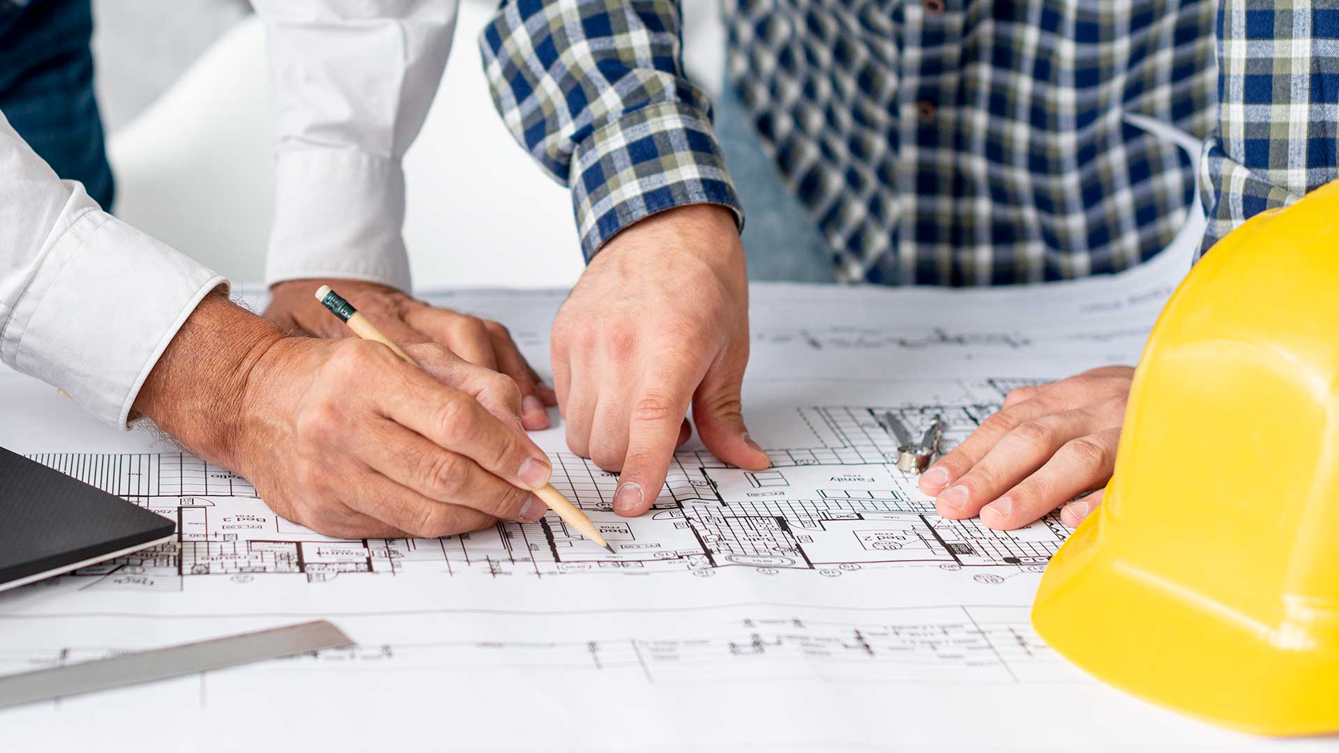 two men are looking at a blueprint with a hard hat in the foreground