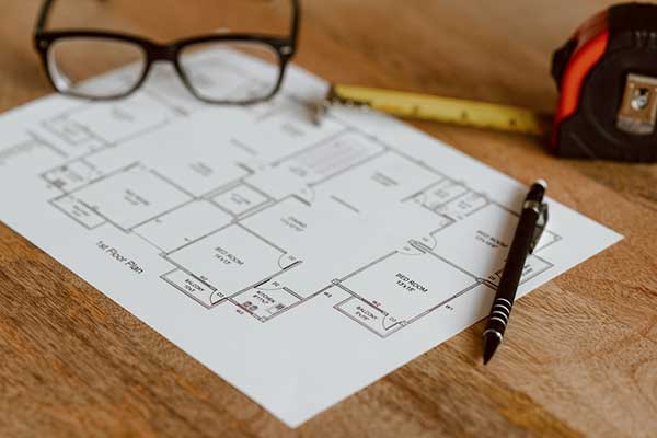a floor plan of a house is sitting on a wooden table next to a pen and glasses