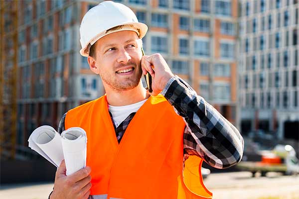a construction worker is talking on a cell phone while holding blueprints .