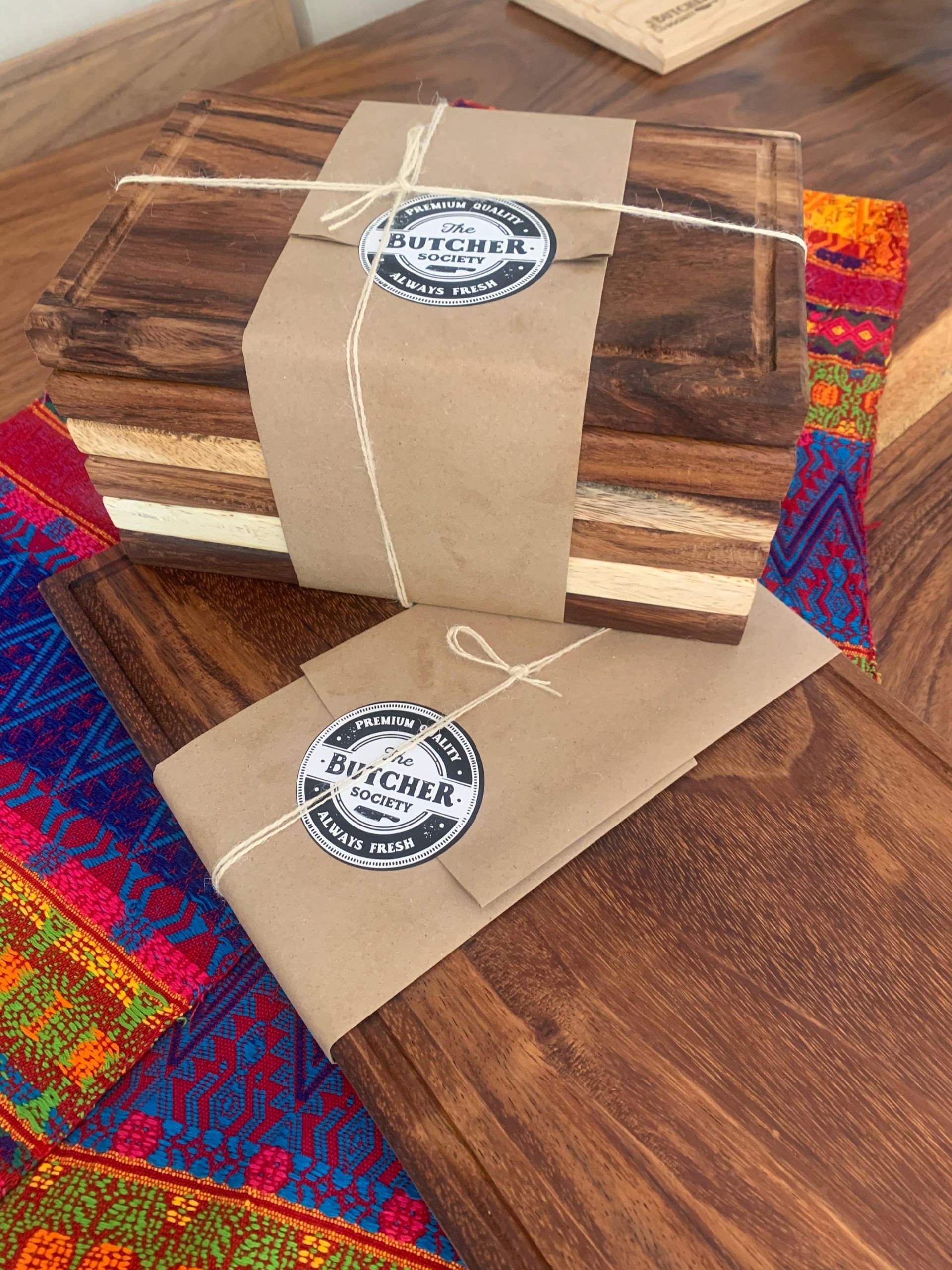 Cajas de madera hechas a mano envueltas con bandas de papel color canela y tela tejida de colores sobre una mesa de madera.