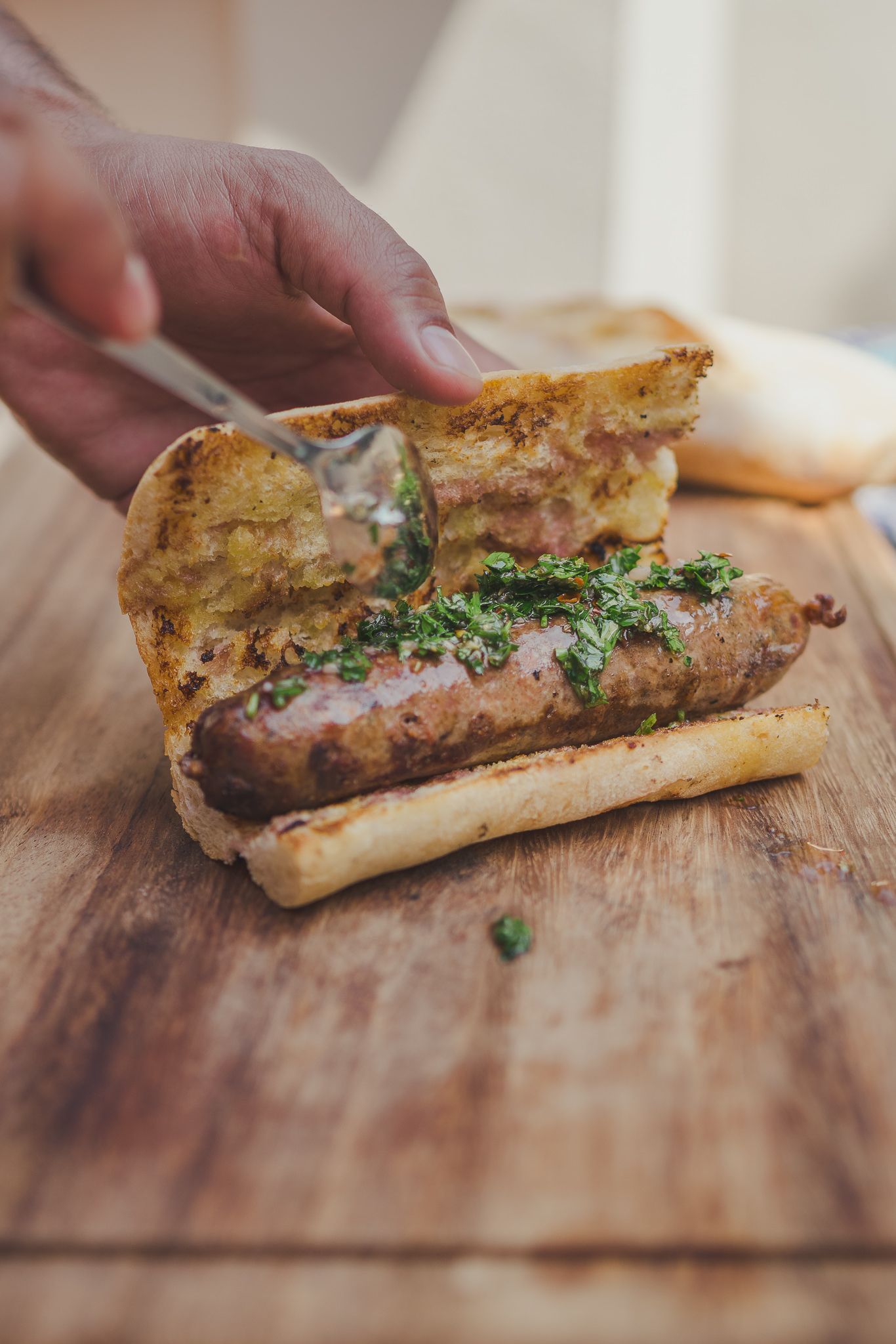 Cortar a mano un sándwich a la parrilla sobre una tabla de madera, cubierto con hierbas.