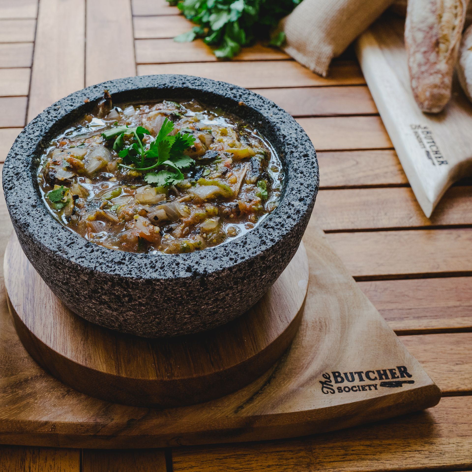 Sopa rústica humeante en un cuenco de piedra sobre una bandeja de madera con guarnición de perejil y pan sobre una mesa.