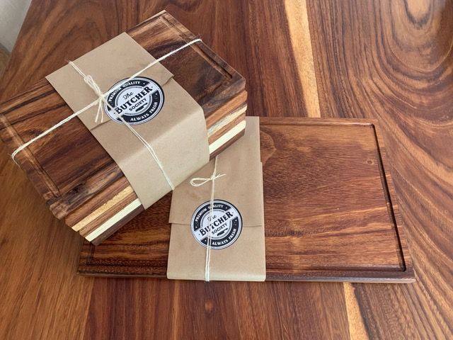 Tablas de cortar de madera envueltas con embalaje marrón y cordel, apiladas sobre una superficie de madera.