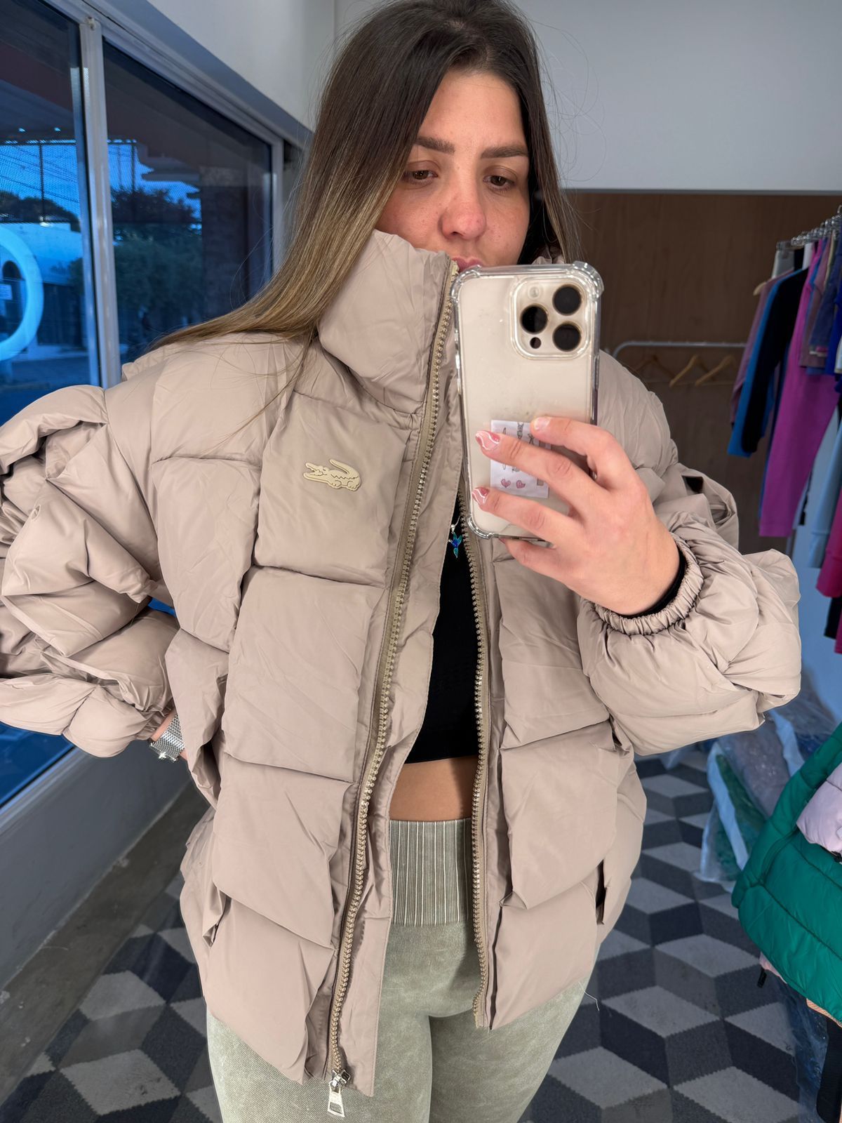 Una persona que viste una chaqueta acolchada Lacoste de color marrón y sostiene un teléfono.