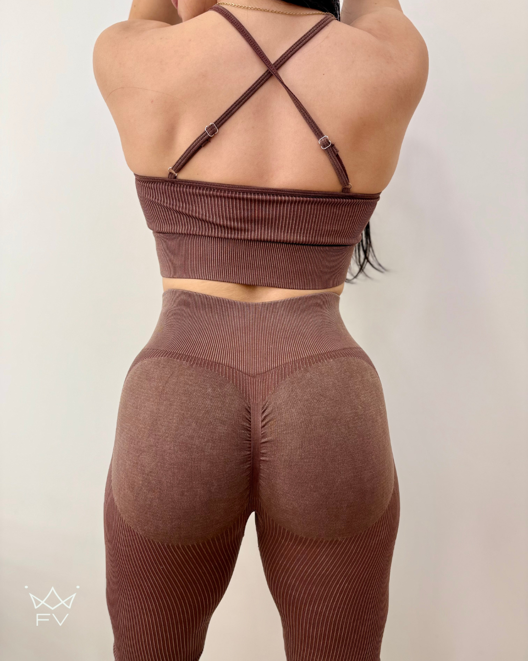 Mujer con un conjunto deportivo de canalé marrón, con top halter y leggings.