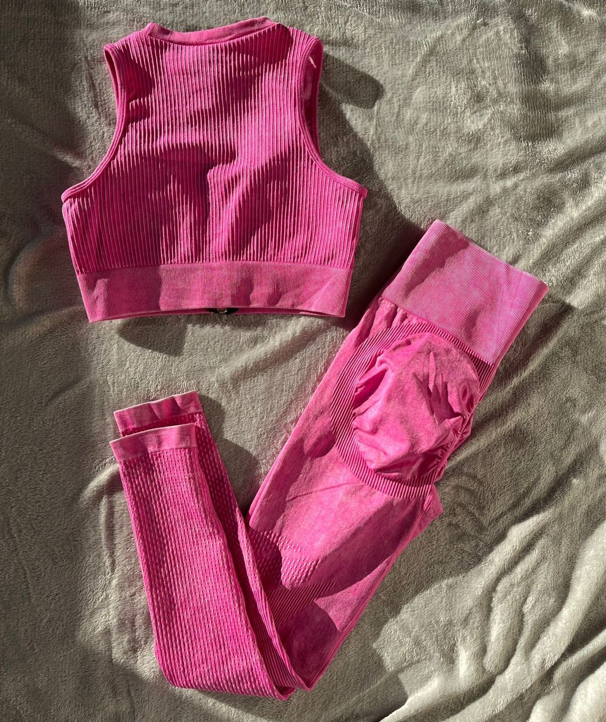Conjunto de entrenamiento de canalé rosa: sujetador deportivo con abertura y cremallera, leggings, sobre superficie arrugada.