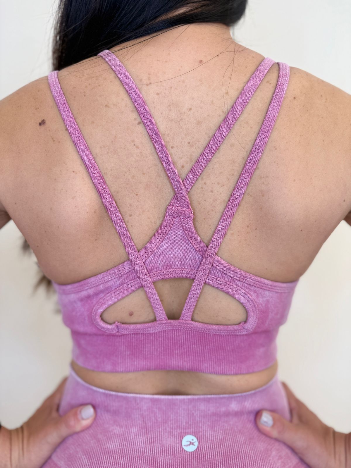 Mujer con conjunto deportivo rosa, con las manos en las caderas y de espaldas a la cámara.