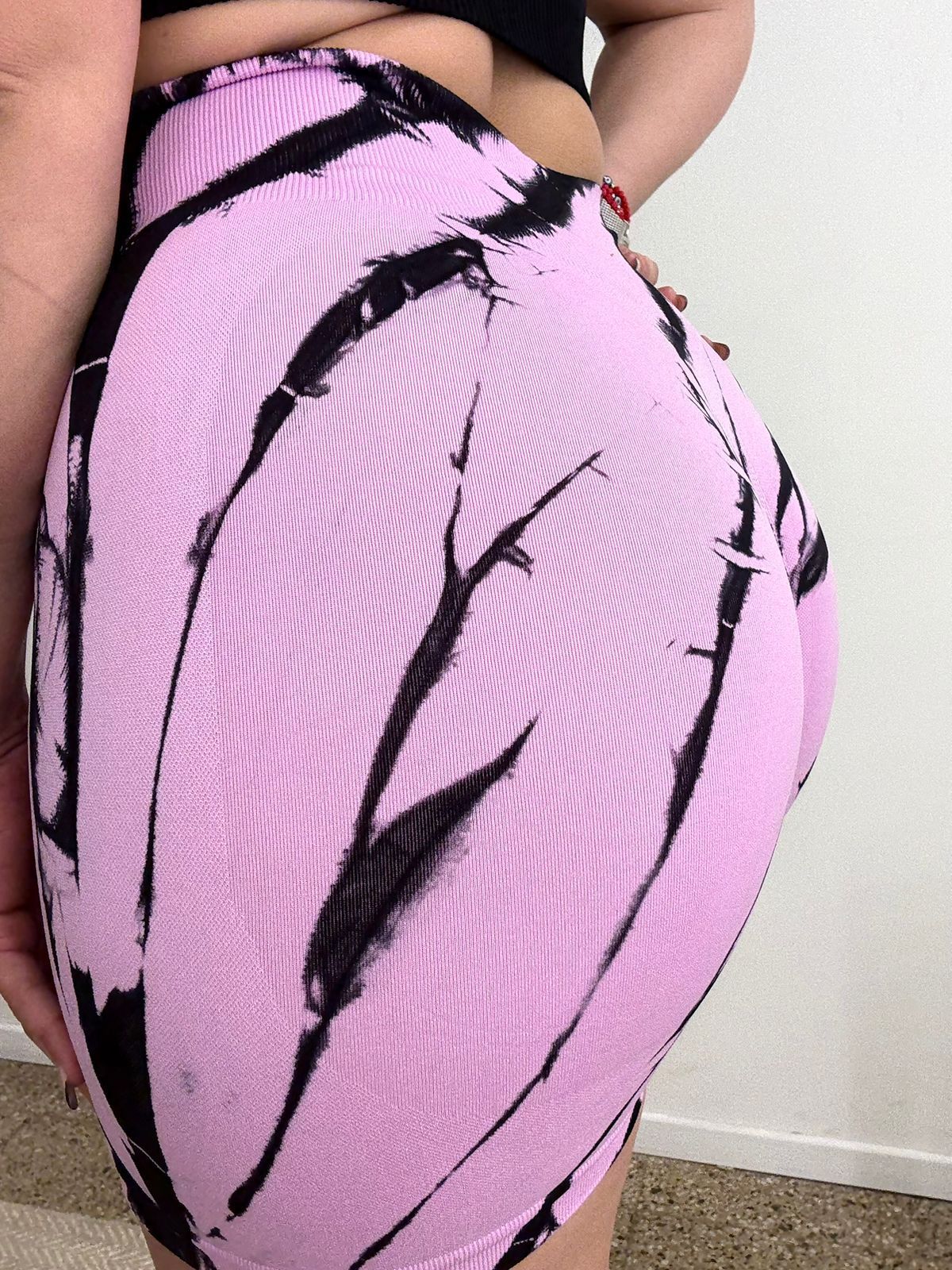 Mujer con pantalones cortos teñidos de color lila con vetas negras, de pie con las manos en las caderas.