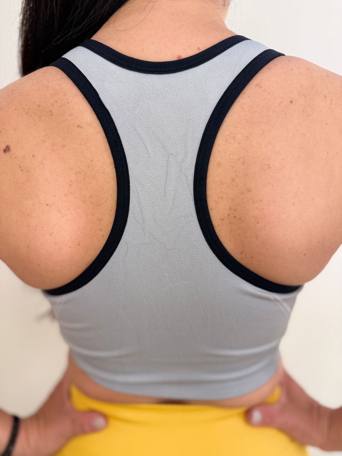 Mujer que lleva un sujetador deportivo gris con cremallera y ribete negros; manos en las caderas.