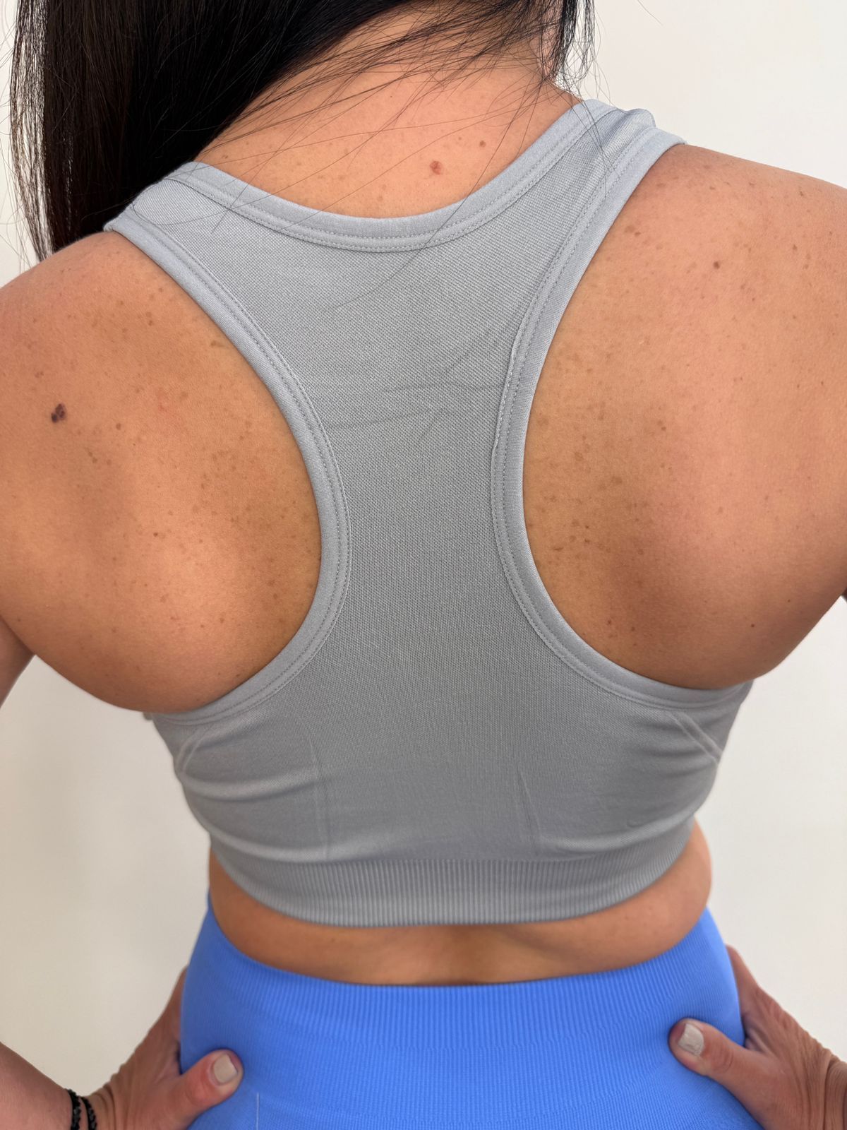 Mujer que viste un sujetador deportivo gris con cremallera frontal y pantalones deportivos azules; entorno interior.