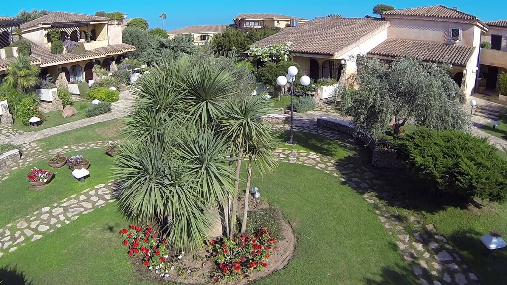 area verde con sentieri in pietra, palme e fiori rossi