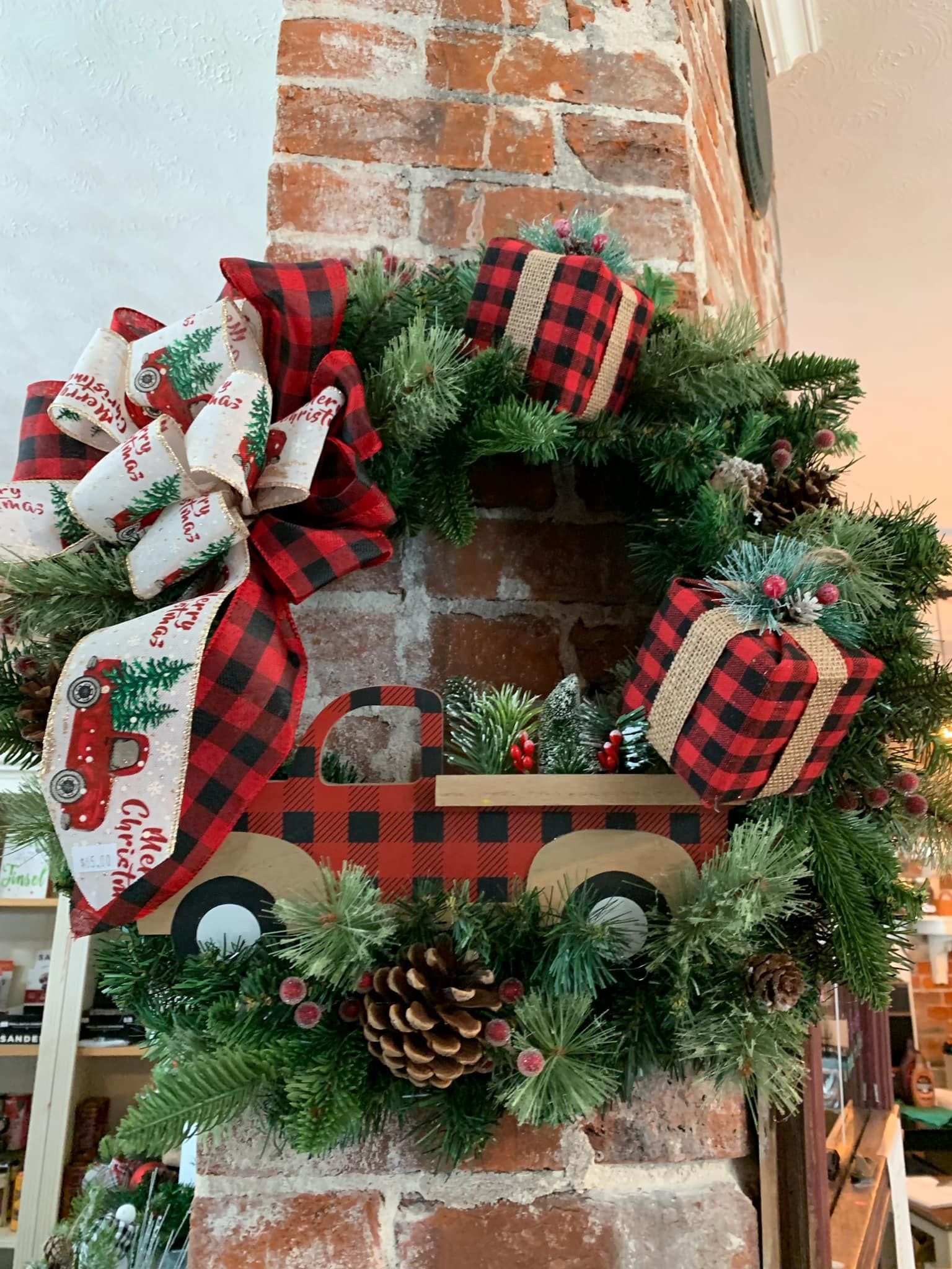 A christmas wreath with a truck and presents on it is hanging on a brick wall.