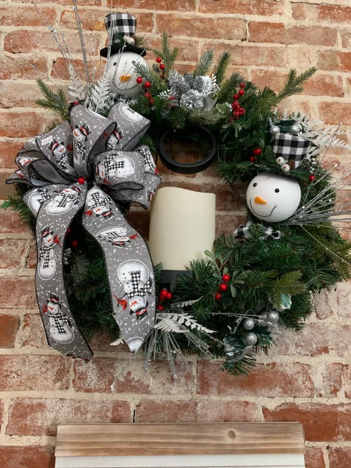 A christmas wreath with snowmen and a candle on a brick wall.