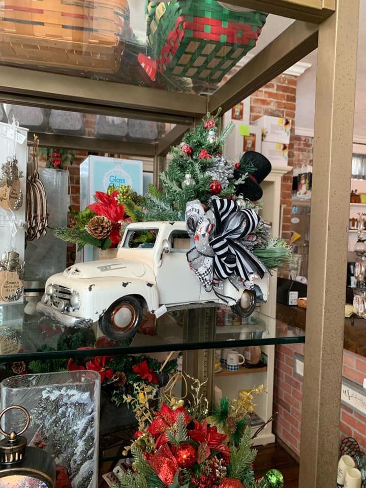 A white truck with a christmas tree in the back is on a glass shelf.