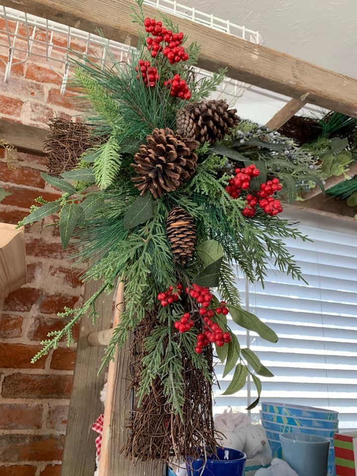 A christmas wreath with pine cones and red berries is hanging on a wooden shelf.