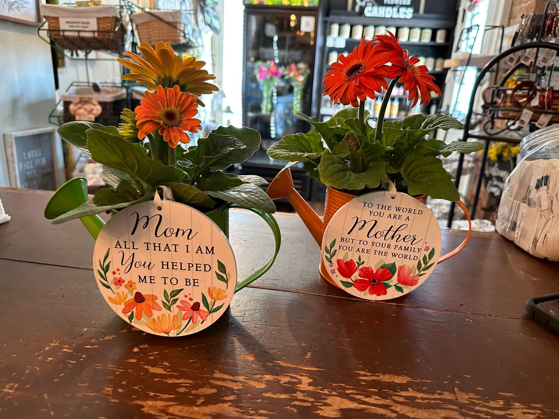 Two watering cans with flowers in them are sitting on a wooden table.