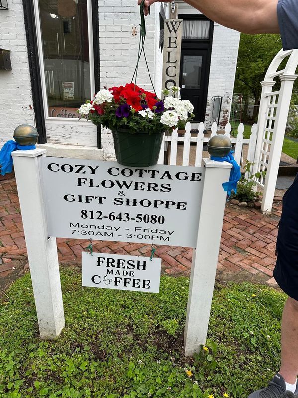 A man is standing in front of a sign that says cozy cottage flowers gift shop