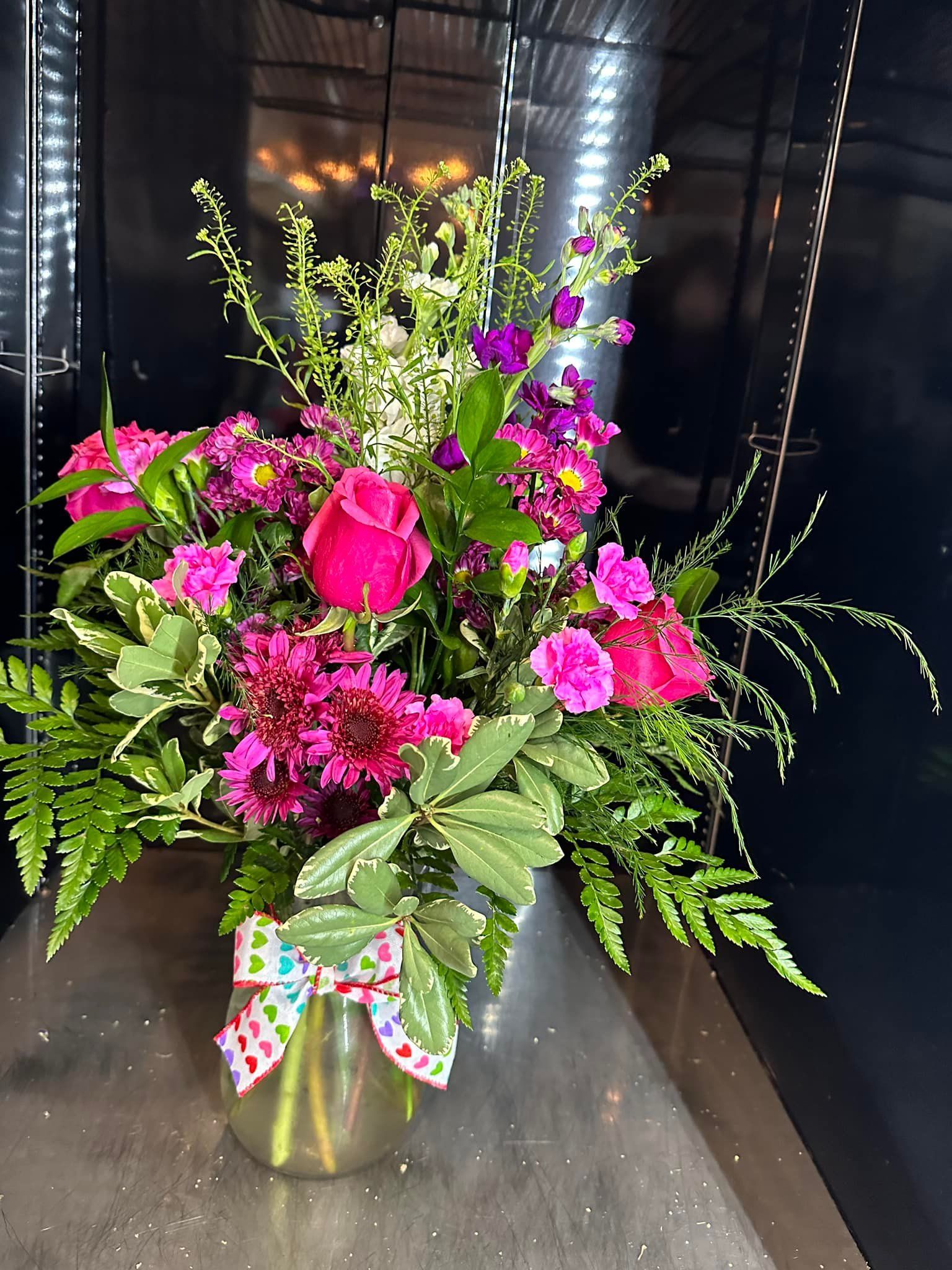 A vase filled with pink flowers and greenery on a table.