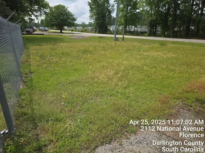 Grassy field next to chain link fence on National Avenue in Florence, South Carolina.