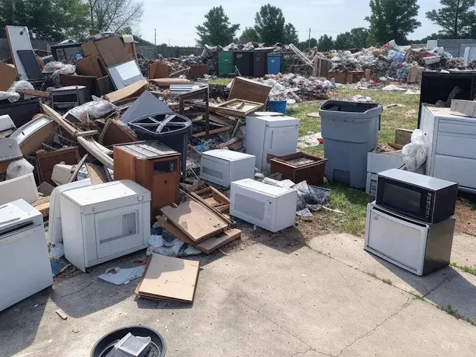 A large pile of discarded appliances and debris in an outdoor area, possibly a dump.