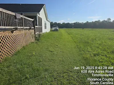 A grassy field with a house on the left. A car is parked in the distance. The date and address are at the bottom.