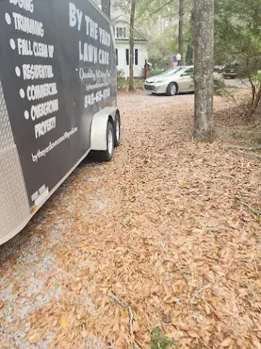 A lawn care trailer parked in a driveway, near a house and car, covered in fallen leaves.