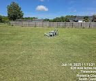 Grassy lot with a fence and small object under a blue sky.