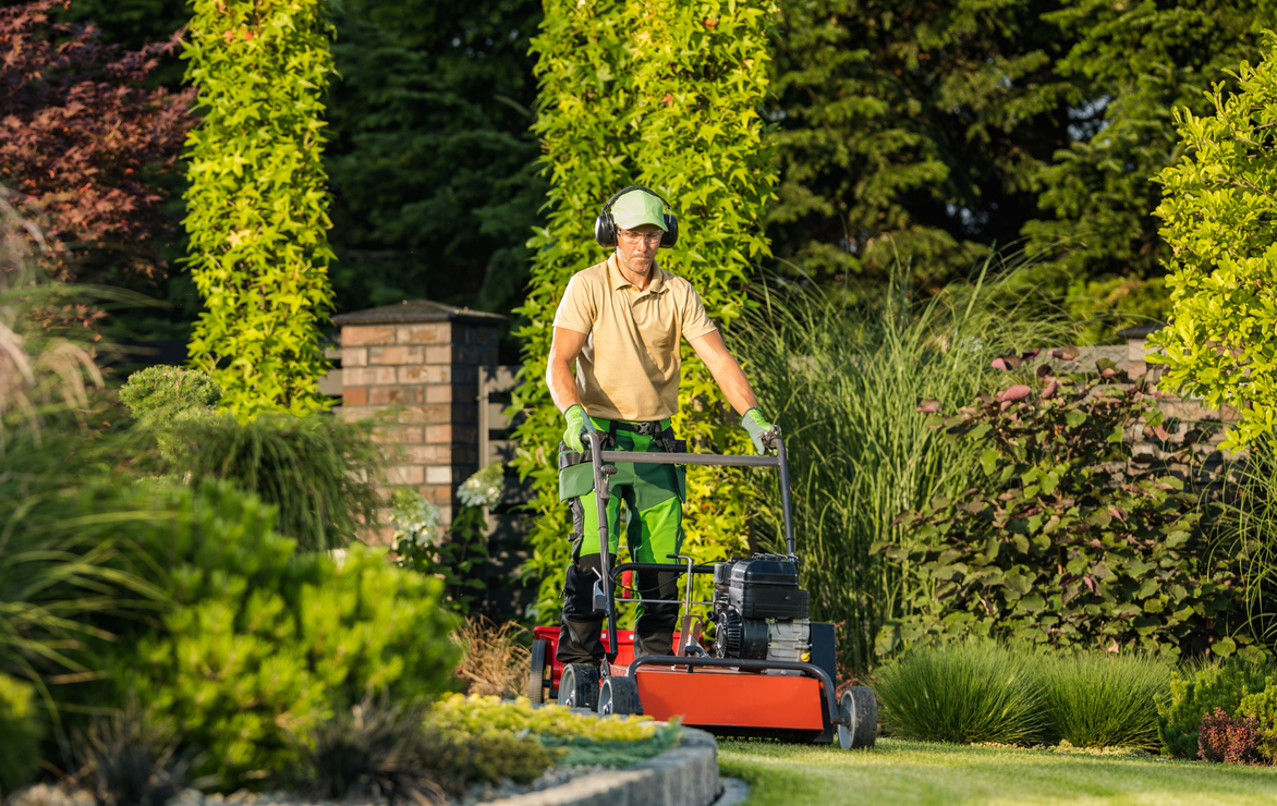 A man mowing a lawn, wearing safety gear, in a well-landscaped garden.