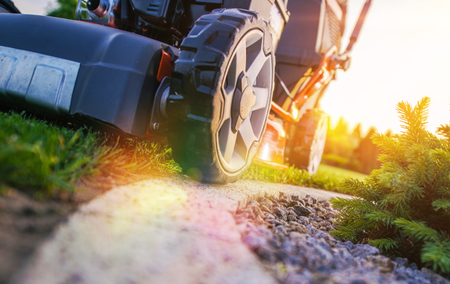 Lawnmower on grass, next to a gravel path, with the sun setting in the background.
