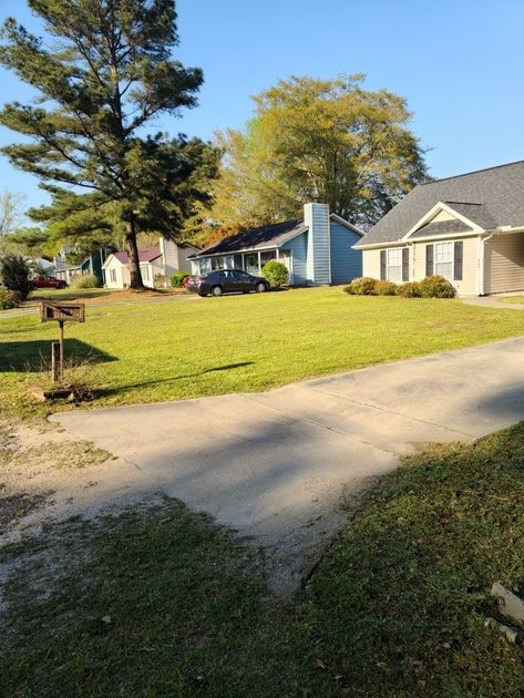 Houses on a sunny day. A car sits parked in front of a light blue house. Green grass and trees in the yard.